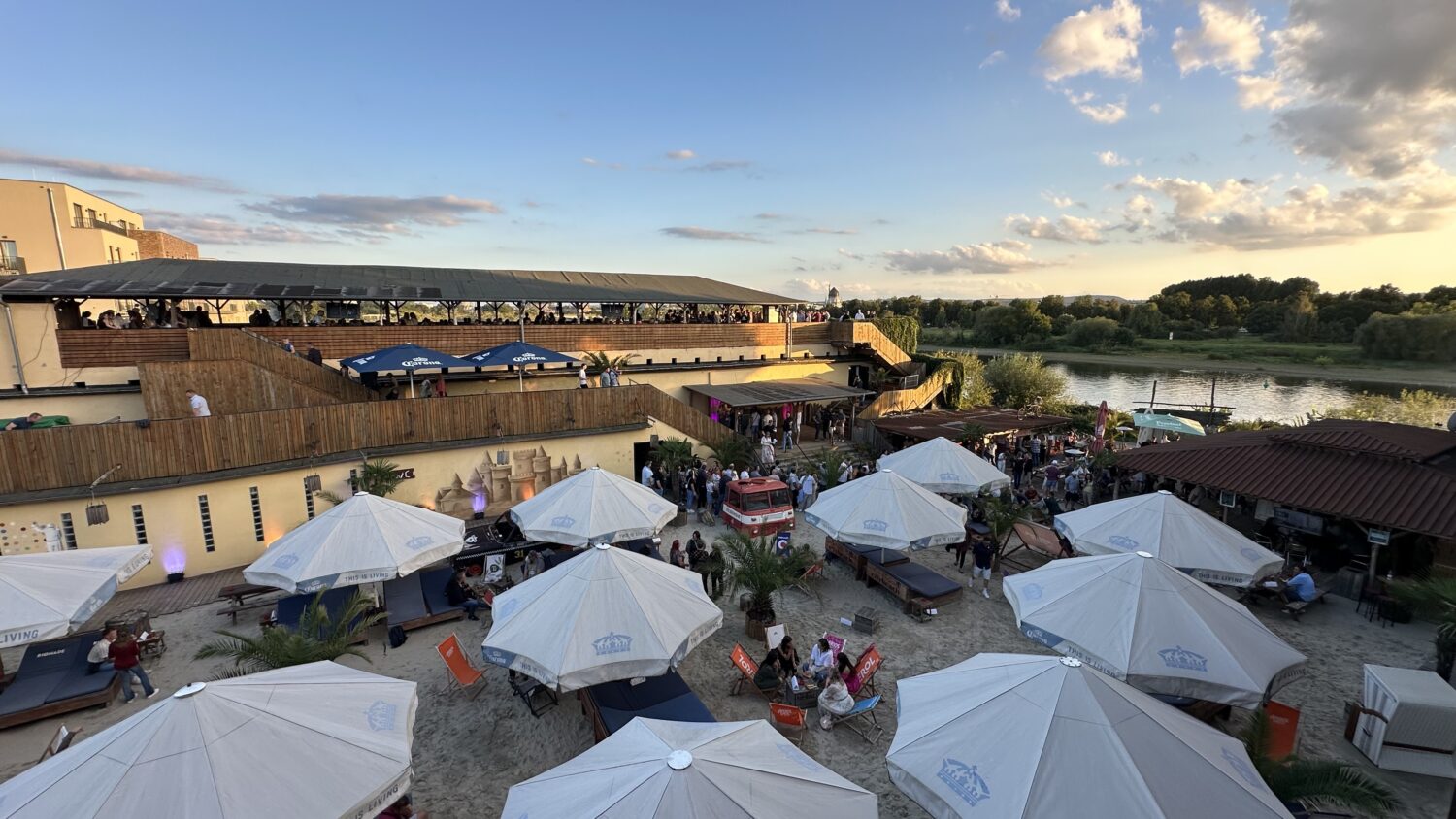 Der Citybeach Dresden aus der Vogelperspektive. Das Foto wurde vom Dach des Bürogebäudes gemacht und zeigt den Citybeach von oben mit dem Eventbereich Dachterrasse, den Sandbereich mit Liegen und Sonnenschirmen, sowie die Elbe.