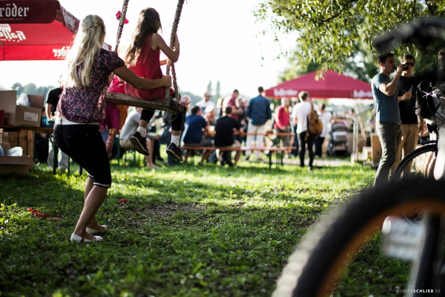 Sommerliche Stimmung auf einer Wiese beim Schreber31-Event 2014 mit einer schaukelnden Person und Besuchern im Hintergrund.