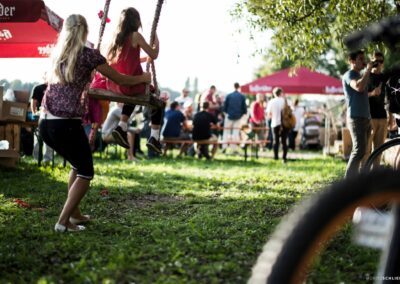 Sommerliche Stimmung auf einer Wiese beim Schreber31-Event 2014 mit einer schaukelnden Person und Besuchern im Hintergrund.