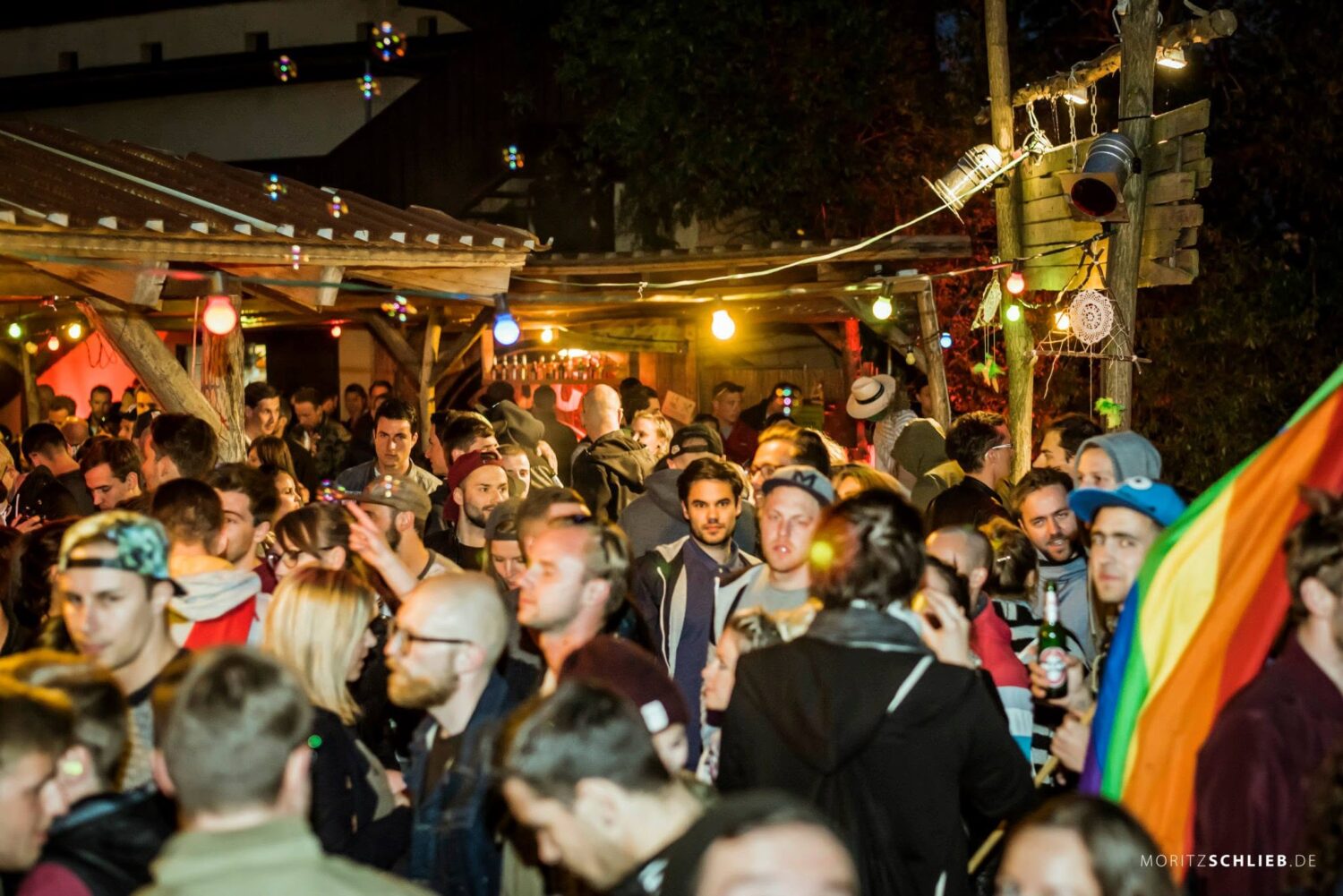 Ausgelassene Party-Stimmung mit vielen Gästen, bunter Beleuchtung und einer Regenbogenflagge bei einer Abendveranstaltung im Schreber31 im Jahr 2015.