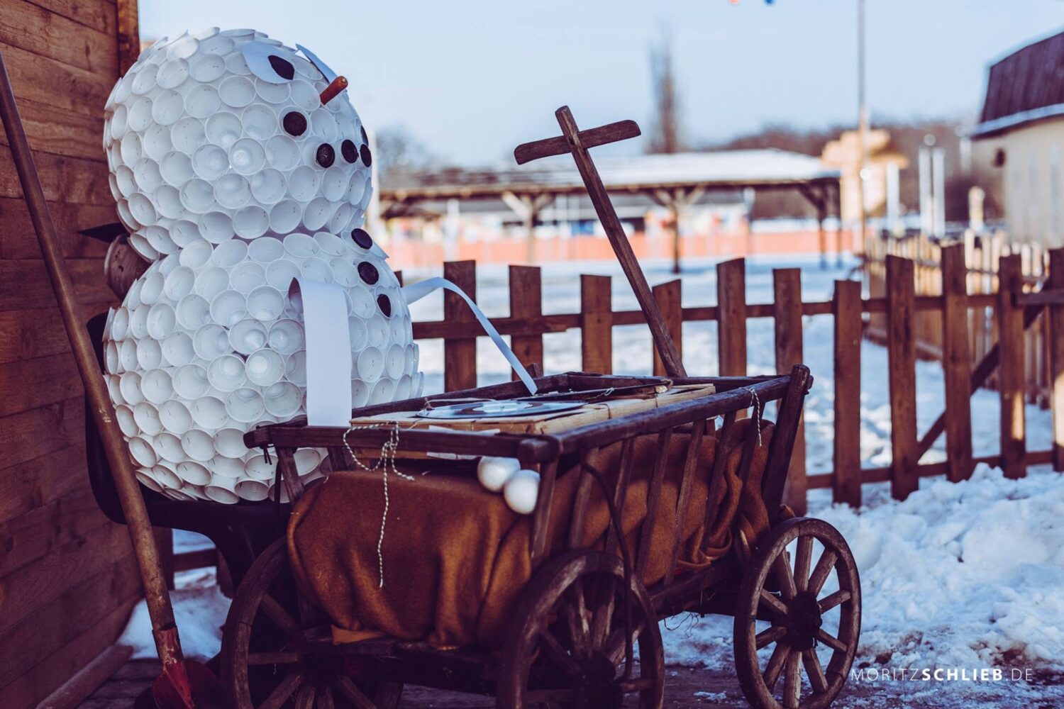 Kreativer Schneemann aus Plastikbechern sitzt vor einem alten Bollerwagen am winterlich verschneiten Citybeach beim Schreber31 im Jahr 2017.
