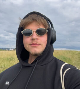 Das Bild zeigt den 23 jährigen Elias im Selbstportait mit Sonnenbrille und Overear-Kopfhörer